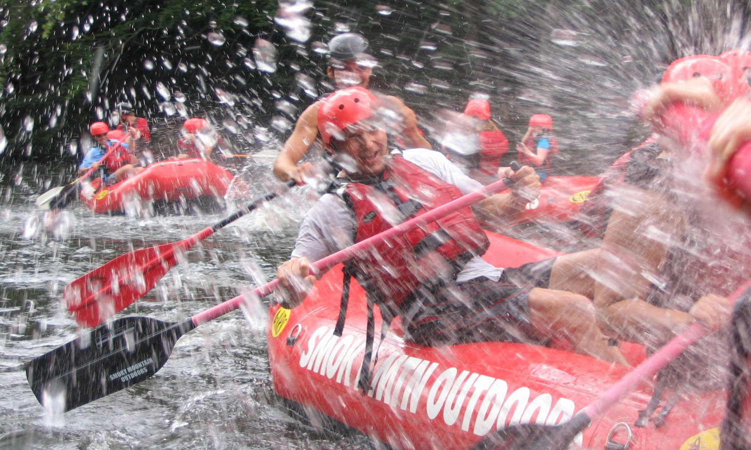 splashing water and people on a red raft with smoky mountain outdoors