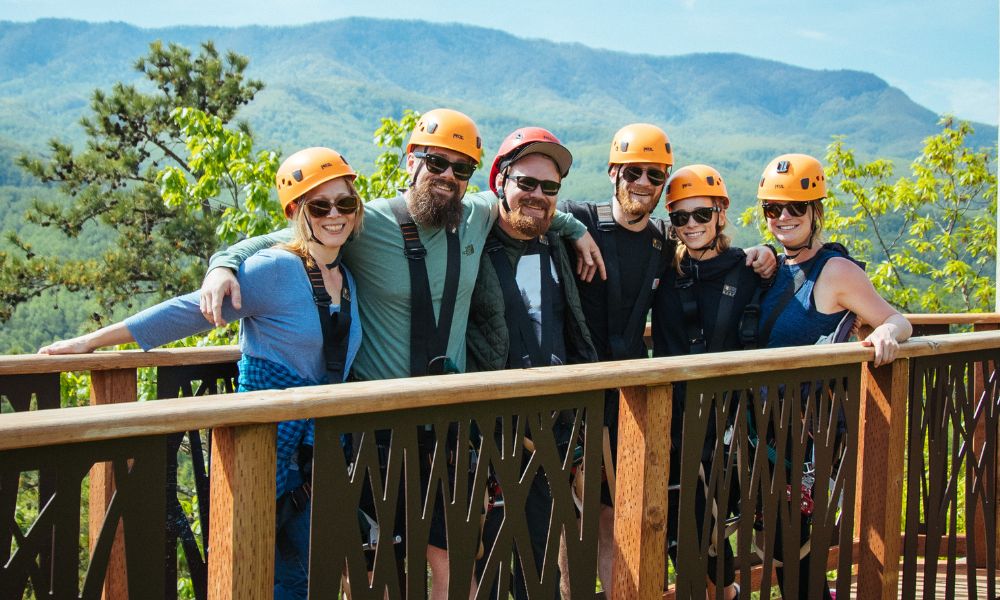 group of people smiling wearing yellow helmets while on a climb works zipline course
