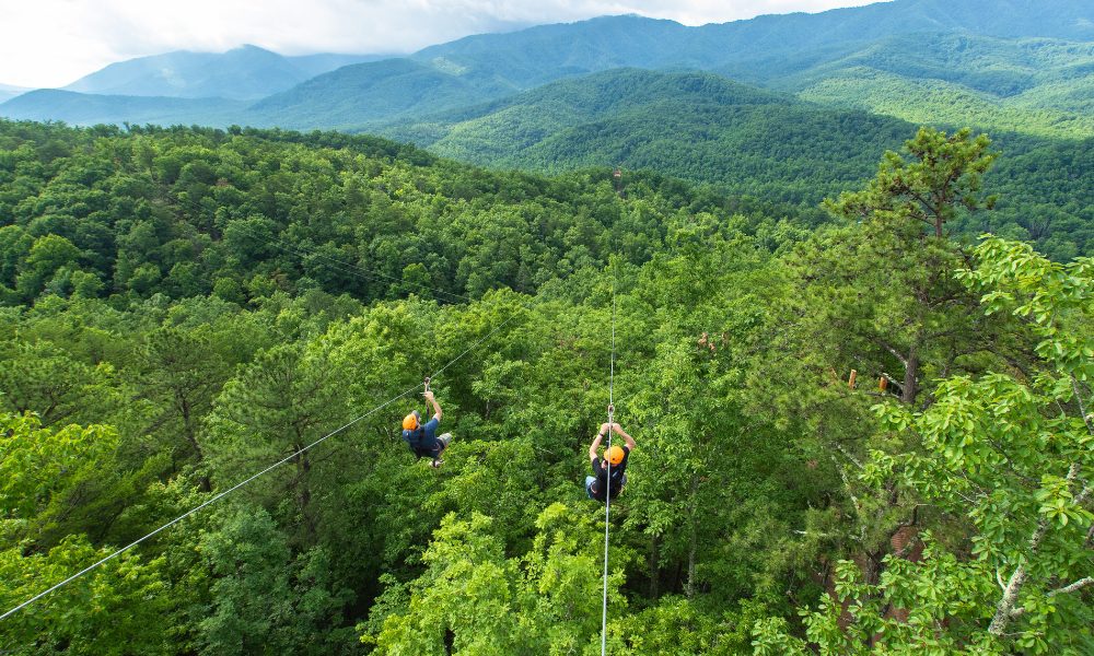 two people zip-lining over the green forests of the smoky mountains